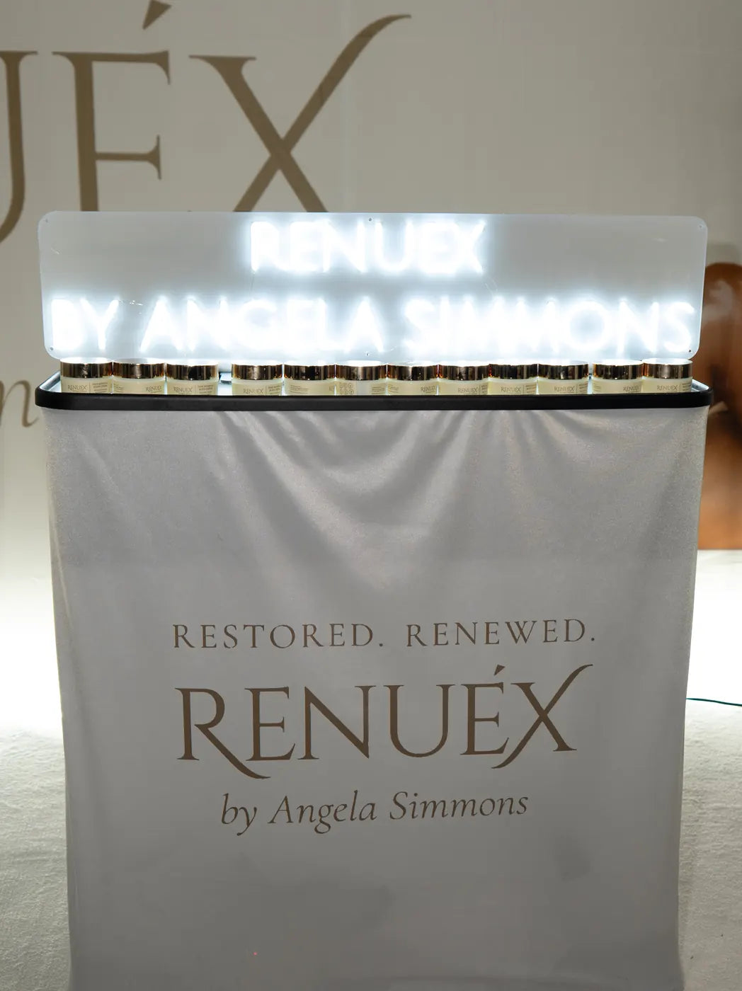 The white neon RENUEX BY ANGELA SIMMONS sign above a row of jars