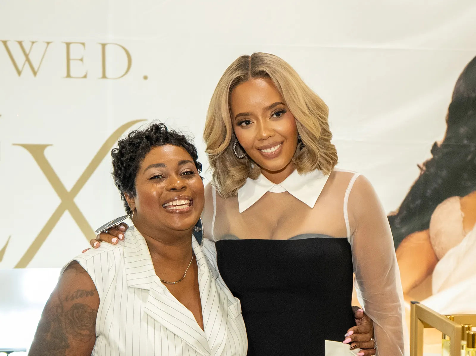 A visitor with her arm around Angela in front of the booth wall